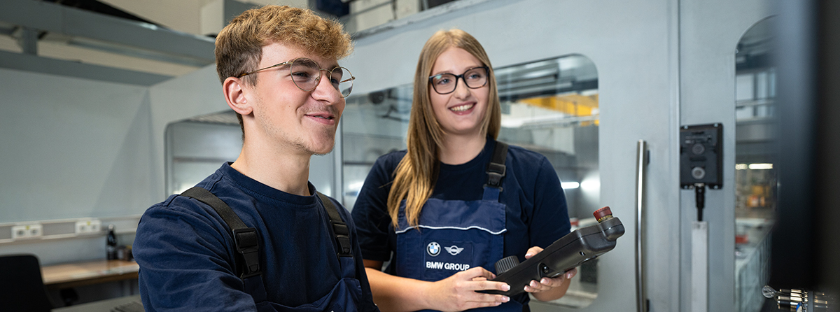 Zwei Auszubildende arbeiten gemeinsam an einer Maschine und Lächeln.