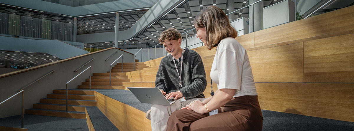 Zwei Studierende der BMW Group unterhalten sich, während sie auf Holzstufen sitzen.