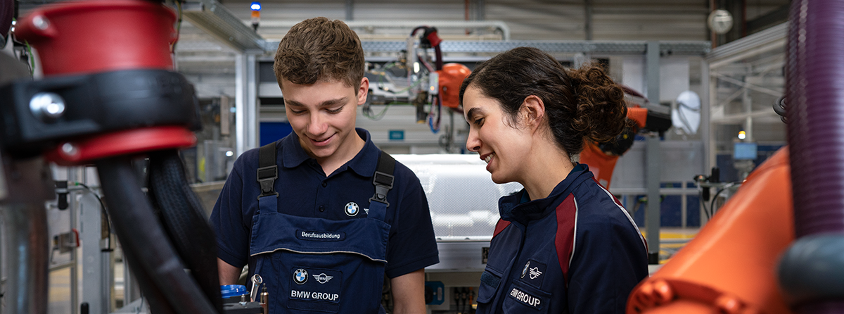 Ein Azubi und seine Ausbilderin in der Produktionshalle.