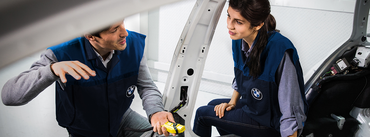 Duale Studentin in Konstruktion bei der BMW Group sitzt in einer Fahrzeugkarosserie und unterhält sich mit ihrem Trainer.