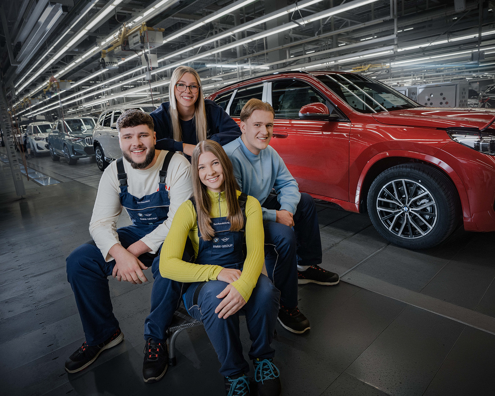 Vier Azubis posen für ein Gruppenfoto in der Montagehalle vor einem roten BMW X1