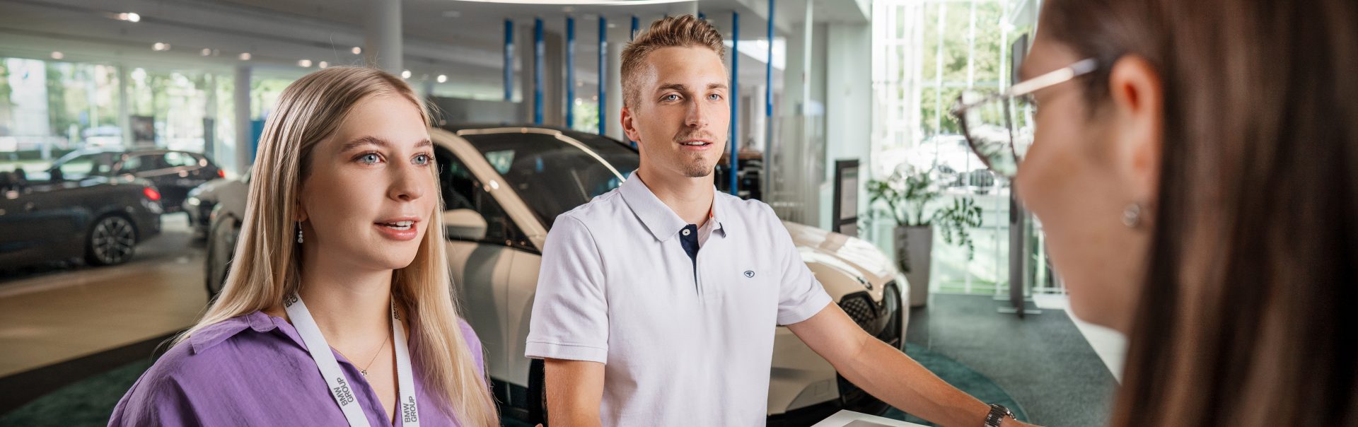 Auszubildende Automobilkaufleute bei BMW mit freundlichem Gesichtsausdruck während einer Beratung.