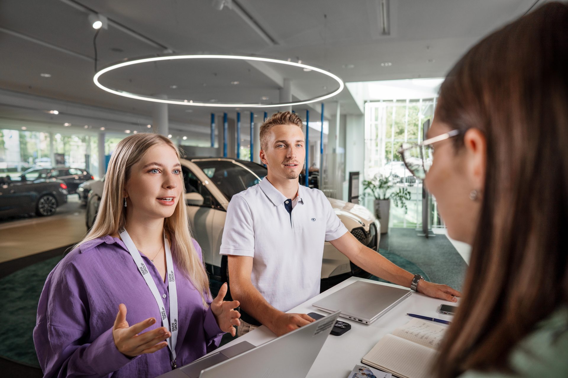 Auszubildende Automobilkaufleute bei BMW mit freundlichem Gesichtsausdruck während einer Beratung.