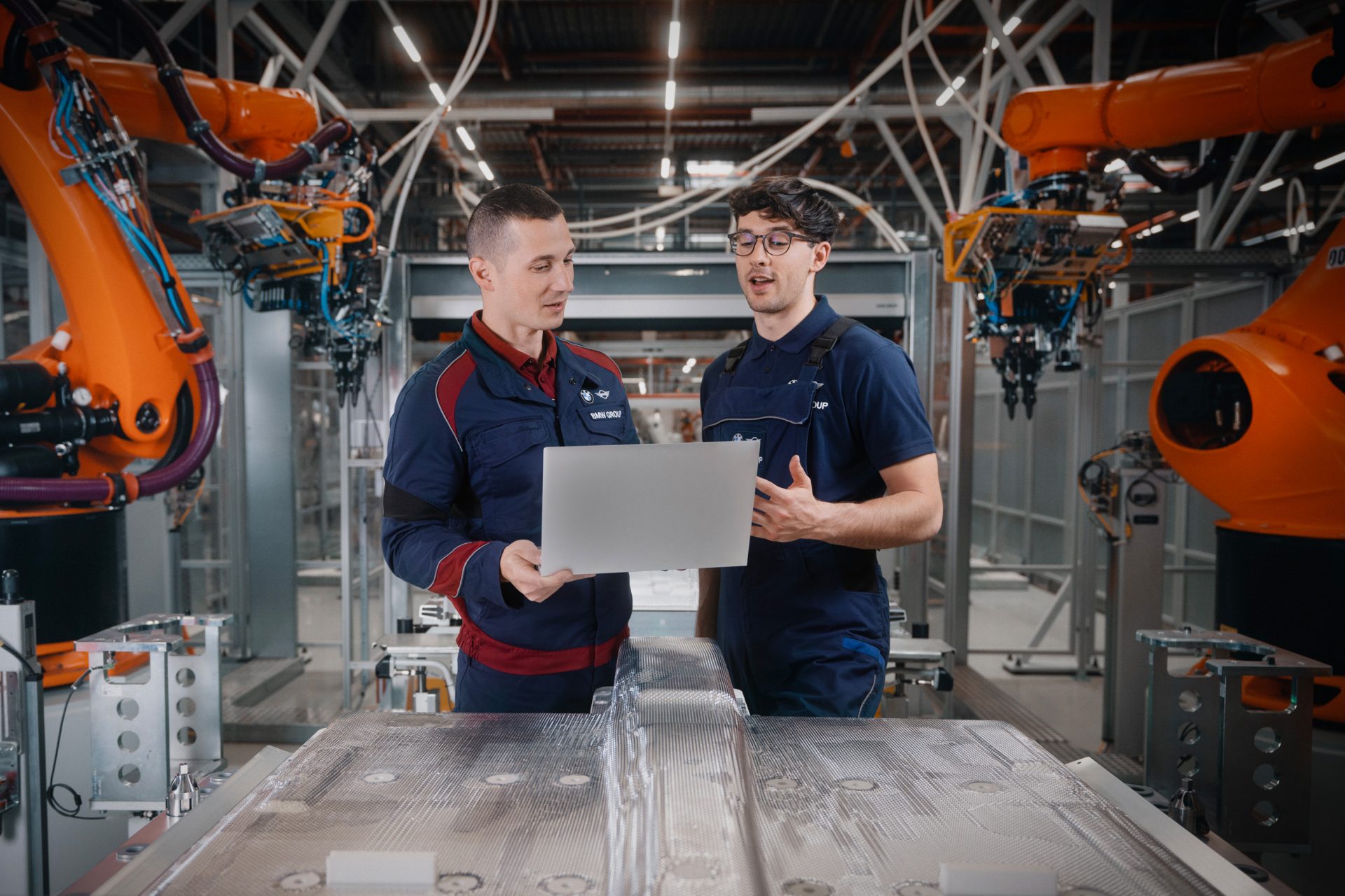 Zwei Auszubildende bei der BMW Group stehen neben einer Maschine und unterhalten sich über etwas auf dem Computer.