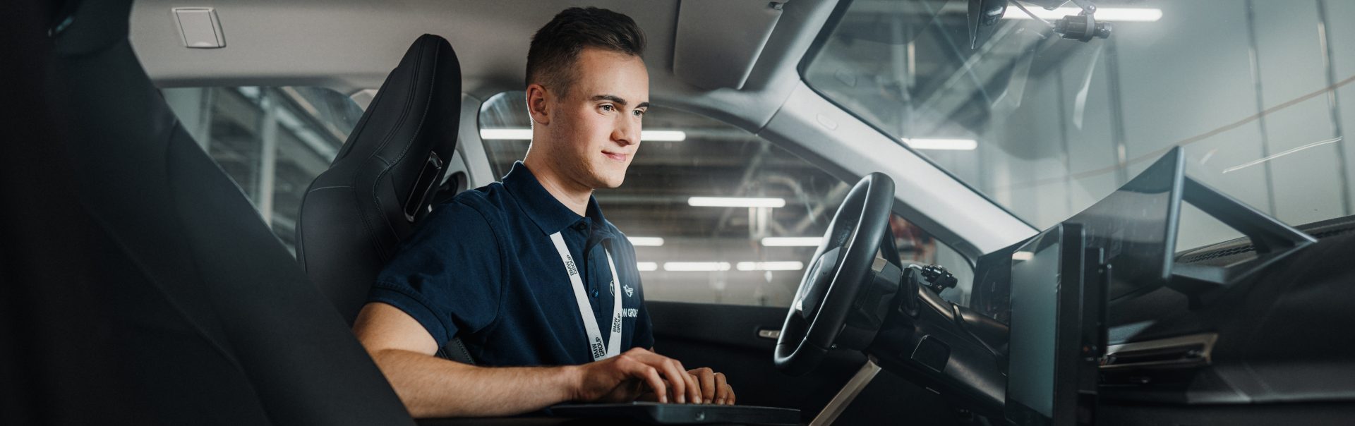 Technisches Setup im Auto mit einem auszubildendem für digitale Vernetzung bei der BMW Group, der an einem Computer arbeitet.