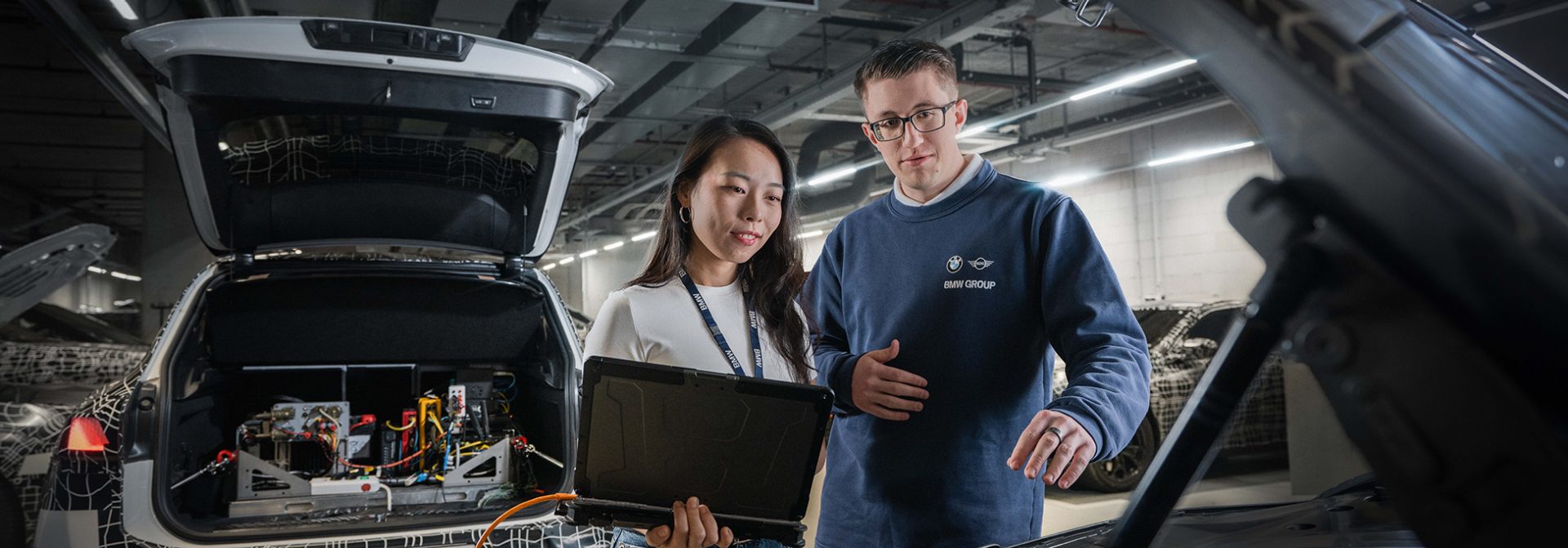 Ein Auszubildender und seine Ausbilderin arbeiten am Heck eines Autos an Elektronik