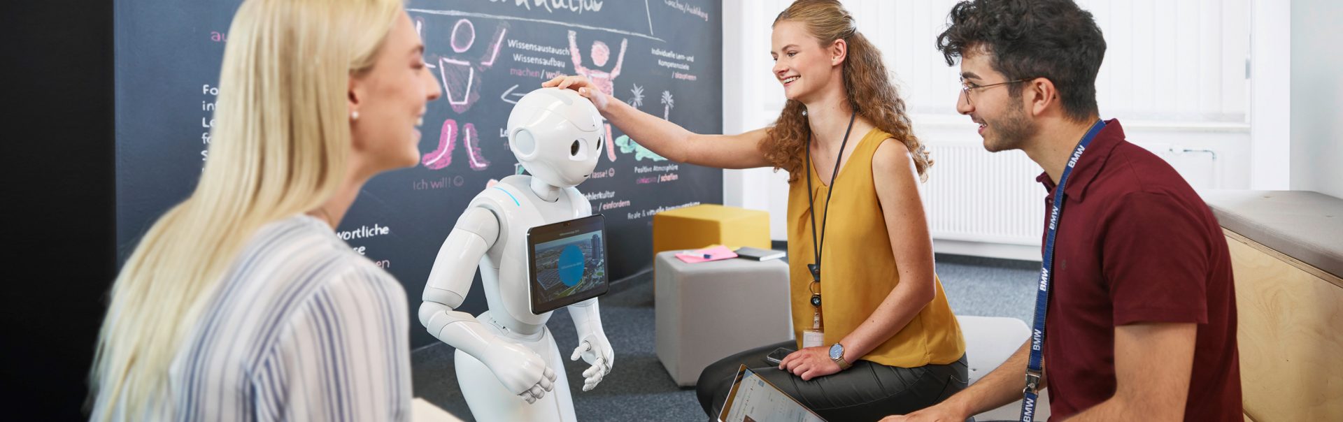 Auszubildende als Fachinformatiker für anwendungsentwicklung bei der BMW Group interagieren mit einem Roboter in einem modernen Büro.