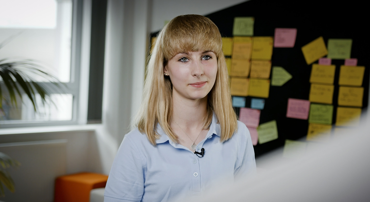 Porträt einer jungen Auszubildenden als Fachinformatikerin für Anwendungsentwicklung bei der BMW Group im Büro mit Haftnotizen im Hintergrund.