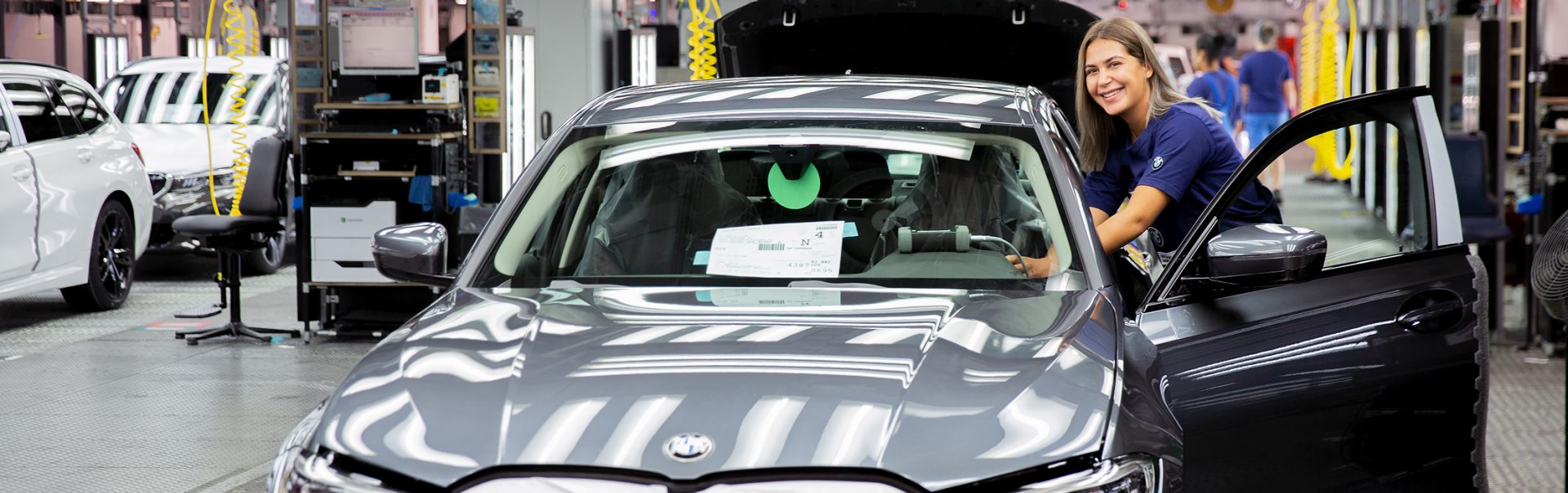 Eine Auszubildende als Fertigungsmechanikerin in der BMW-Fertigung, die an einem neuen Fahrzeug arbeitet.