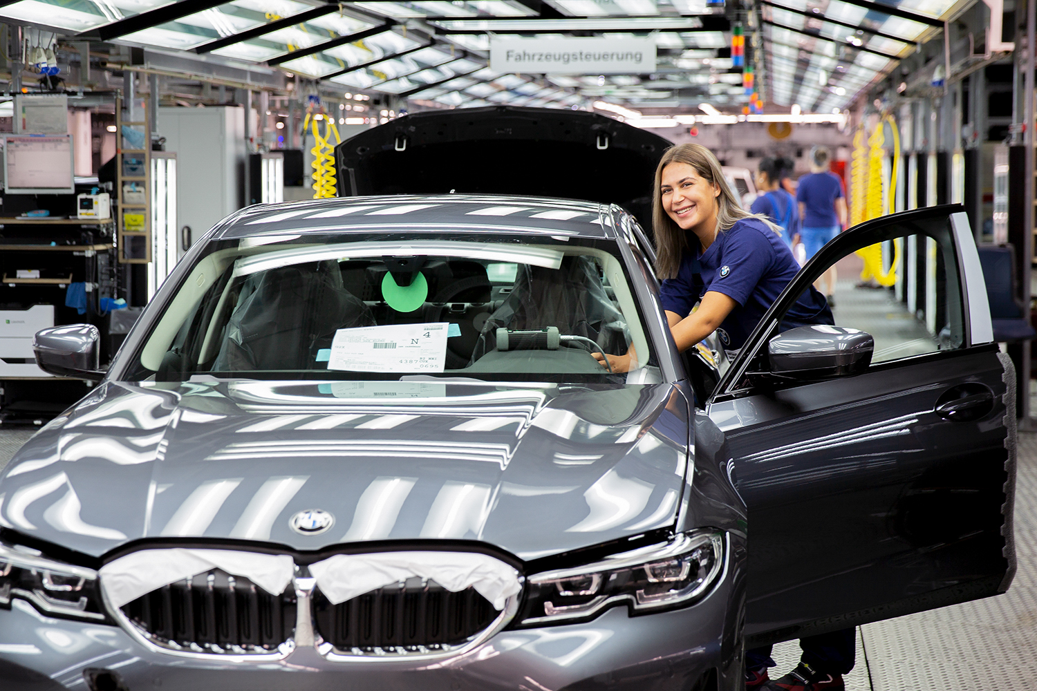 Eine Auszubildende als Fertigungsmechanikerin in der BMW-Fertigung, die an einem neuen Fahrzeug arbeitet.