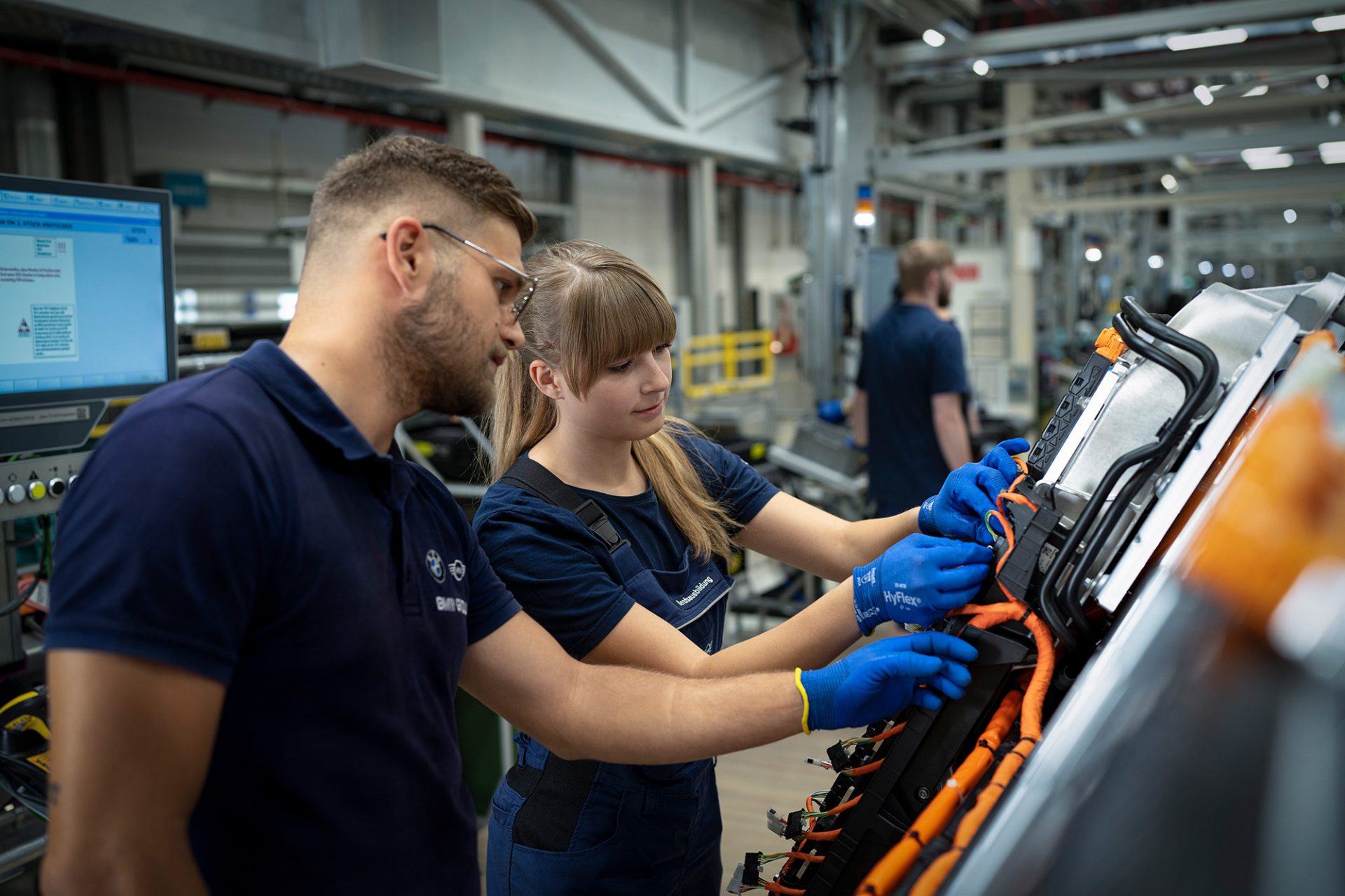 Eine Auszubildende als Fertigungsmechanikerin in der BMW-Fertigung, die an einem neuen Fahrzeug arbeitet.