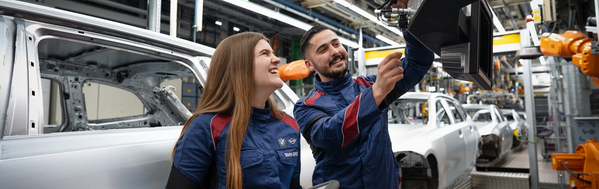 Teamarbeit zwischen Industriemechanikern in einer modernen Autofabrik der BMW Group mit Mitarbeitern, die an einem Fahrzeug arbeiten.