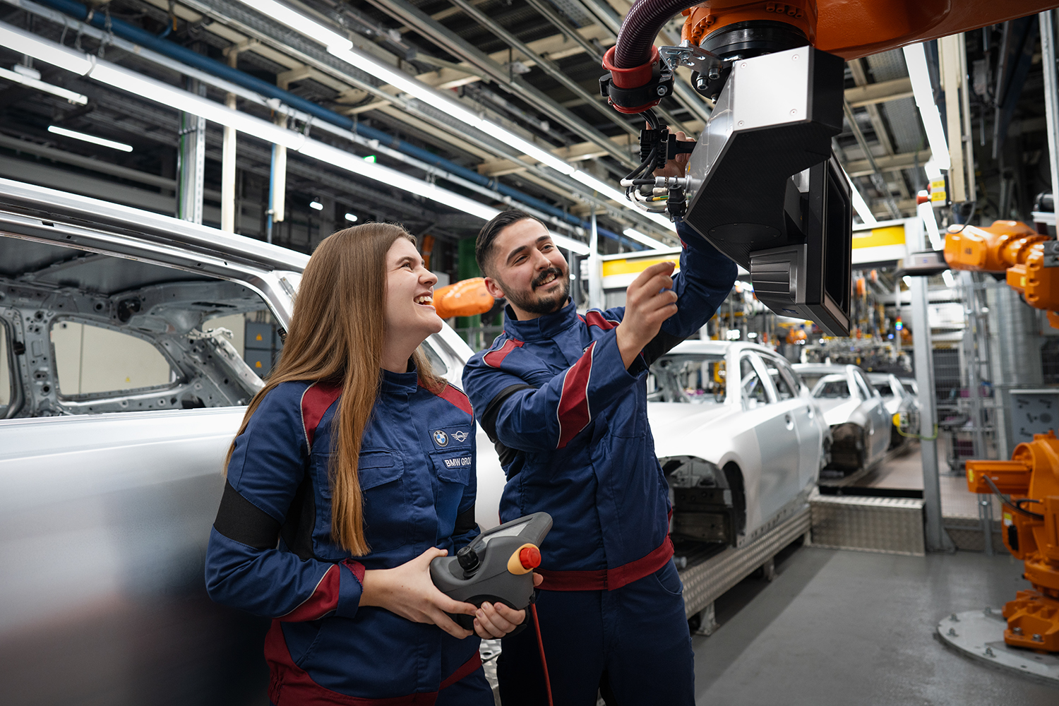 Teamarbeit zwischen Industriemechanikern in einer modernen Autofabrik der BMW Group mit Mitarbeitern, die an einem Fahrzeug arbeiten.