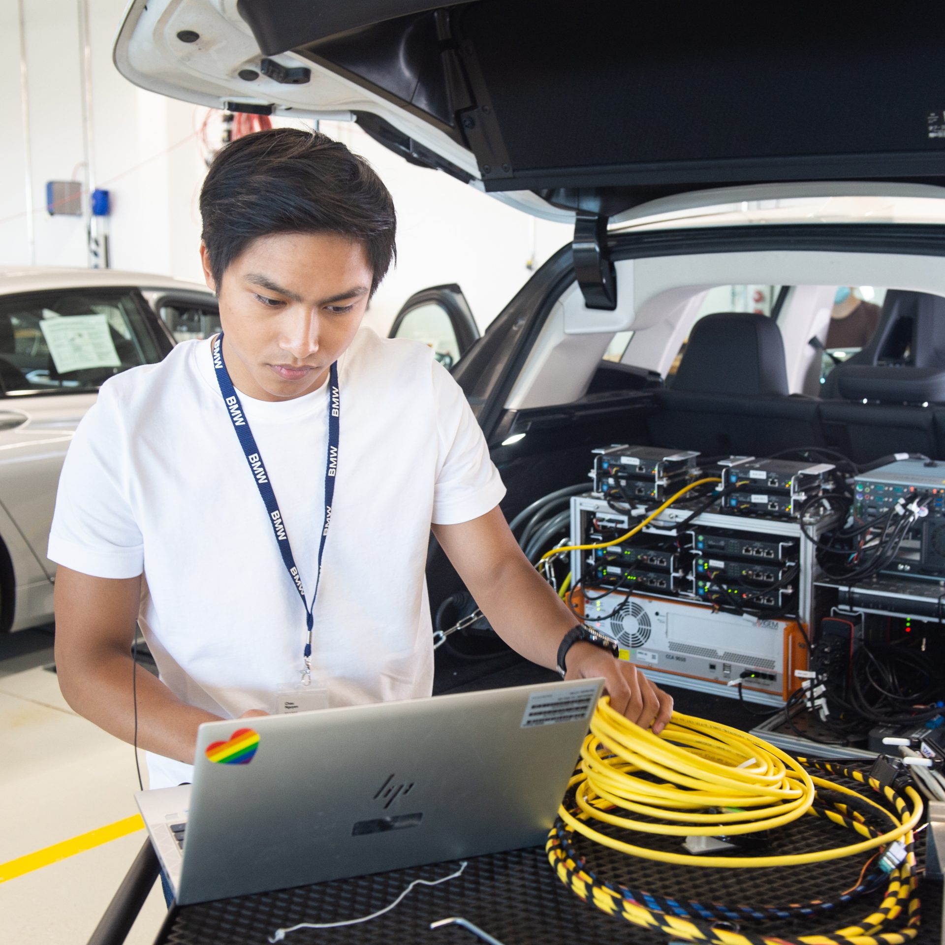 Ein Dualer Student bei der BMW Group mit Fahrzeugdiagnose-Setup im Kofferraum eines BMWs.