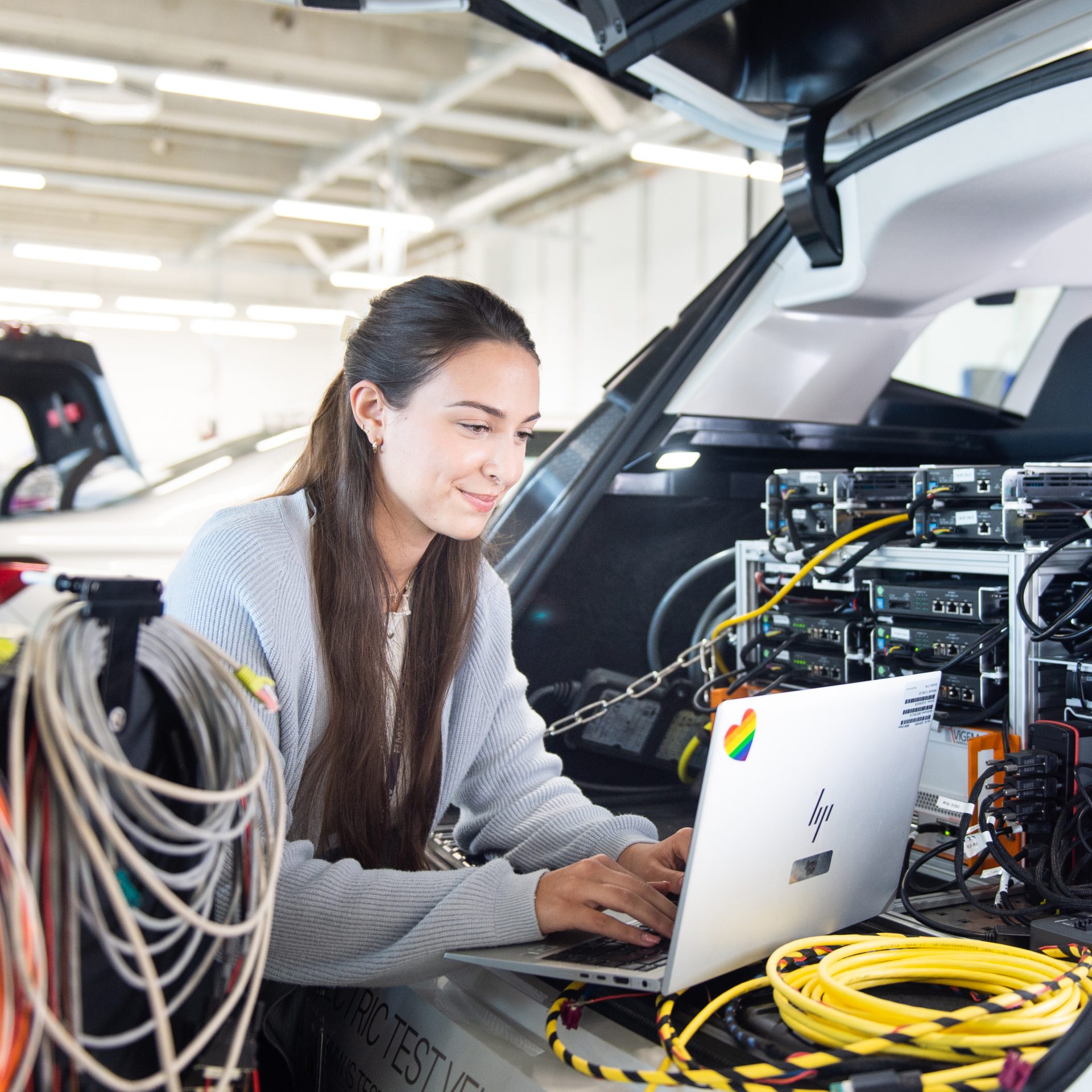 Eine junge Auszubildende führt Diagnosen an einem BMW mit einem Laptop durch.