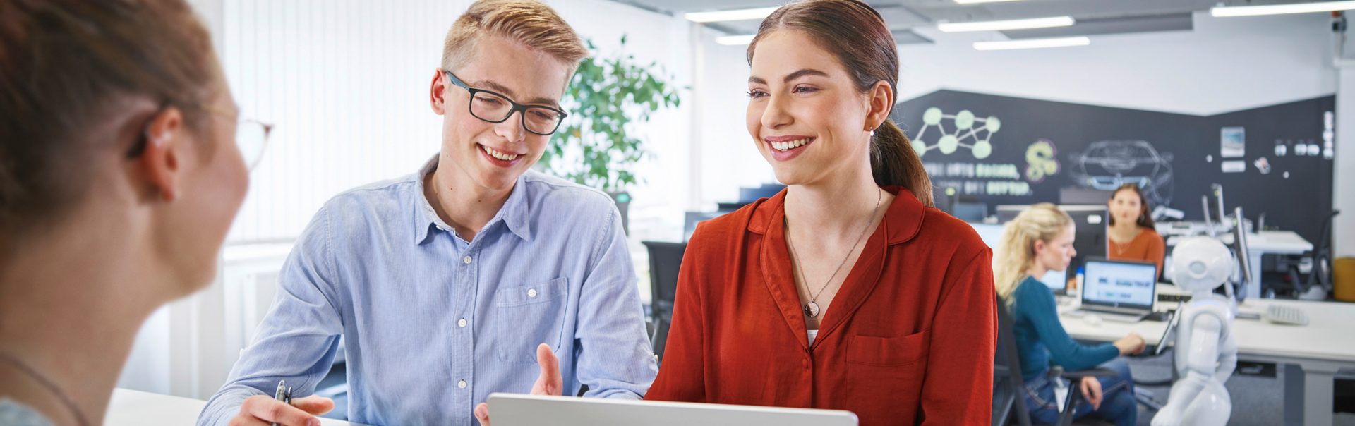 Teamarbeit zwischen drei Kaufmännern für Digitalisierungsmanagement mit Technologie in einem modernen Büro mit Robotern bei der BMW Group.