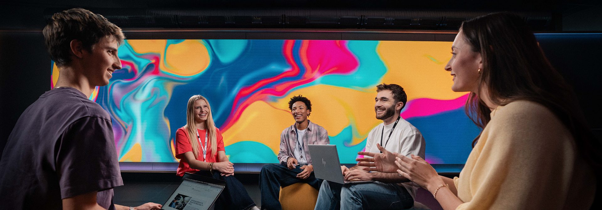 Fünf Azubis haben eine angeregte Unterhaltung vor einem großen Screen mit bunten Farben