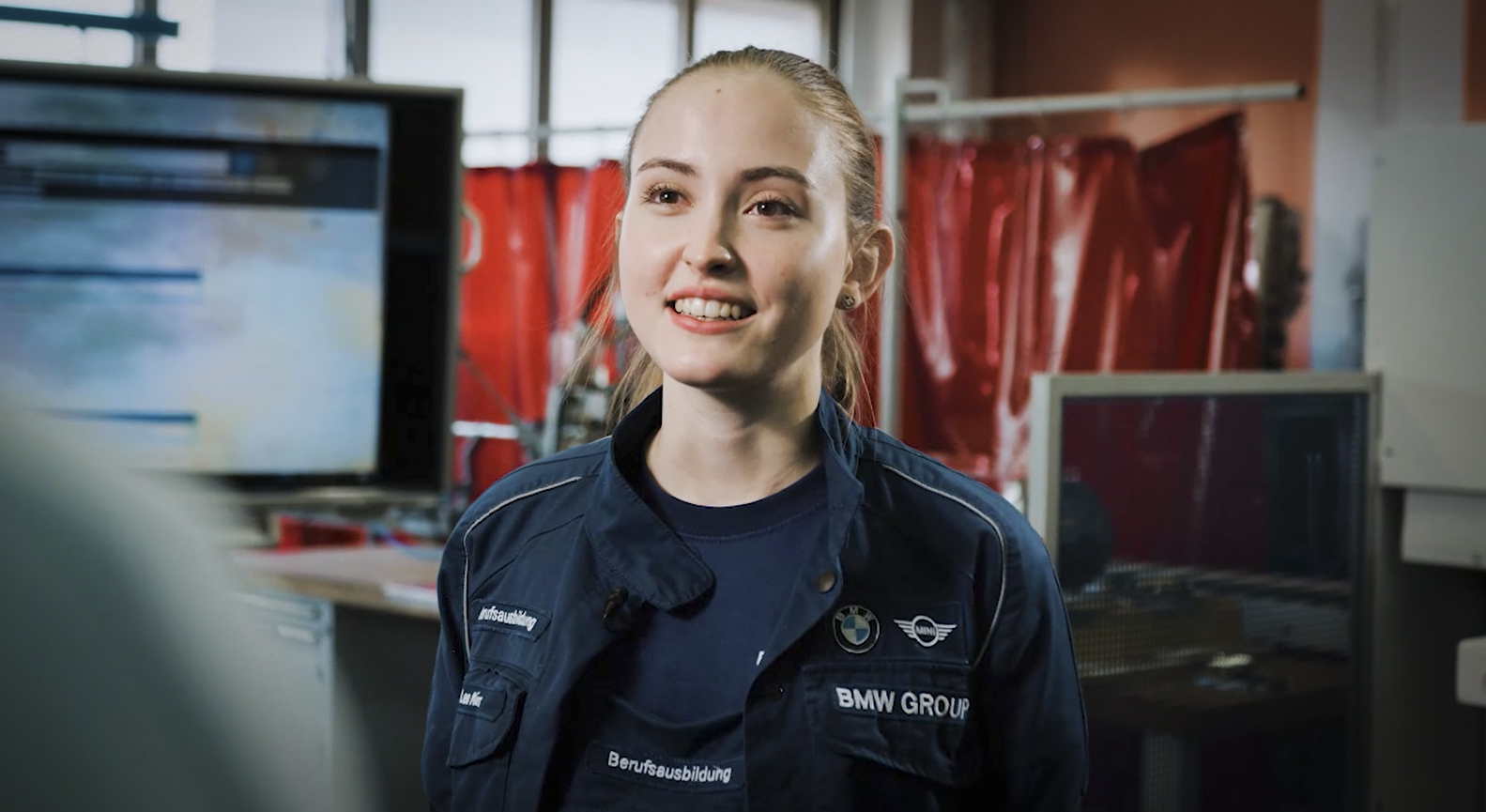 Junge Frau in der Ausbildung zur Karosserie- und Fahrzeugbaumechanikerin bei der BMW Group, lächelnd und engagiert.