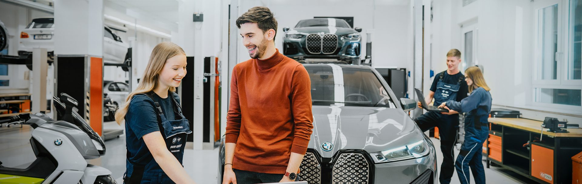Junge auszubildende KFZ-Mechatronikerinnen und Mechatroniker arbeiten in einer BMW-Werkstatt.