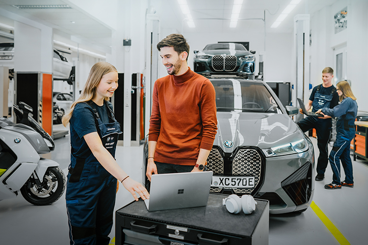 Junge auszubildende KFZ-Mechatronikerinnen und Mechatroniker arbeiten in einer BMW-Werkstatt.
