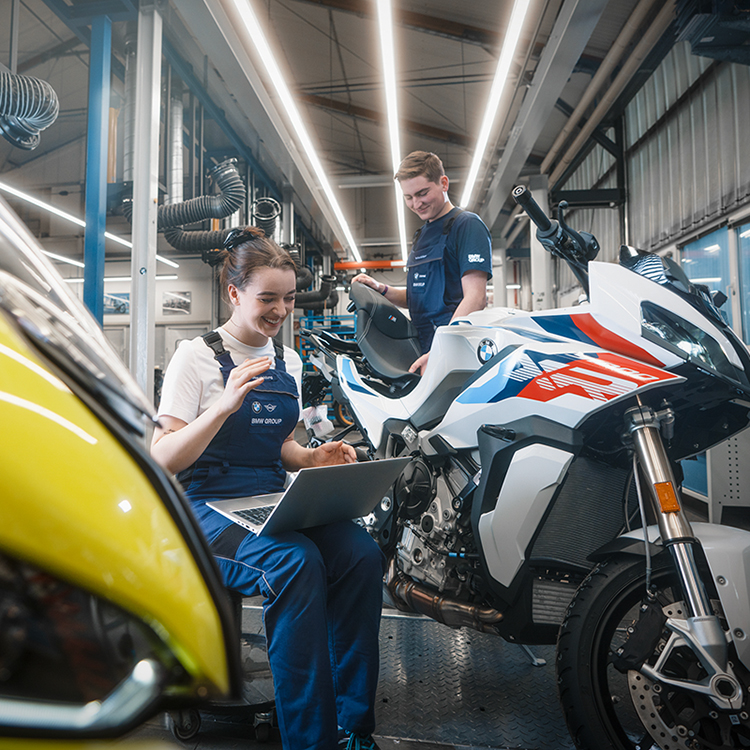 Zwei Mechaniker in einer BMW Motorradwerkstatt arbeiten an einem Motorrad.
