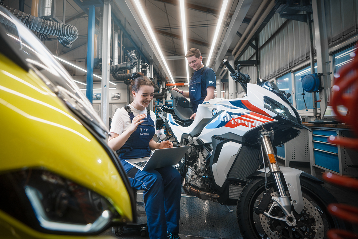 Zwei Auszubildende Motorradtechniker in einer BMW Motorradwerkstatt arbeiten an einem Motorrad.