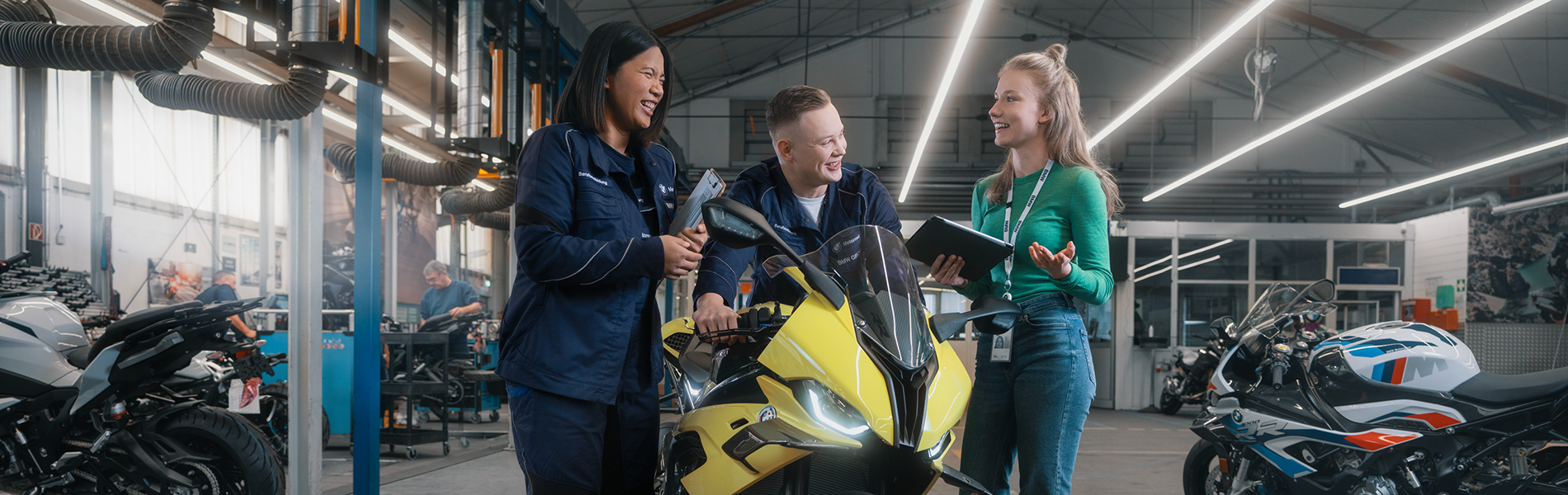 Drei Auszubildende stehen neben einem Motorrad und lachen.