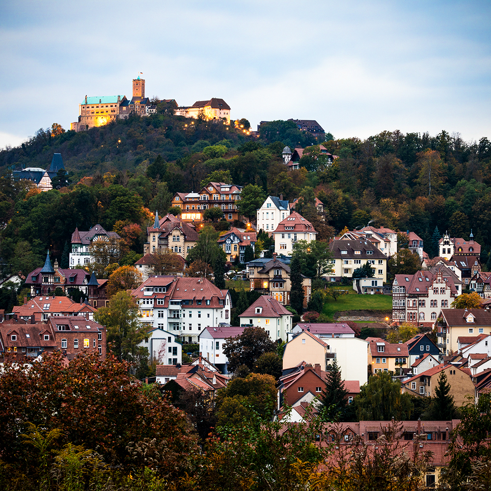 Luftaufnahme der Stadt Eisenach mit einer beleuchteten Burg auf dem Berg.