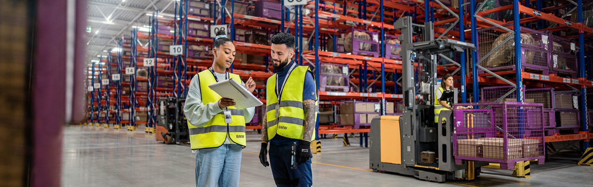 Zwei Logistik-Spezialist:innen schauen auf ein Klemmbrett im Warenlager