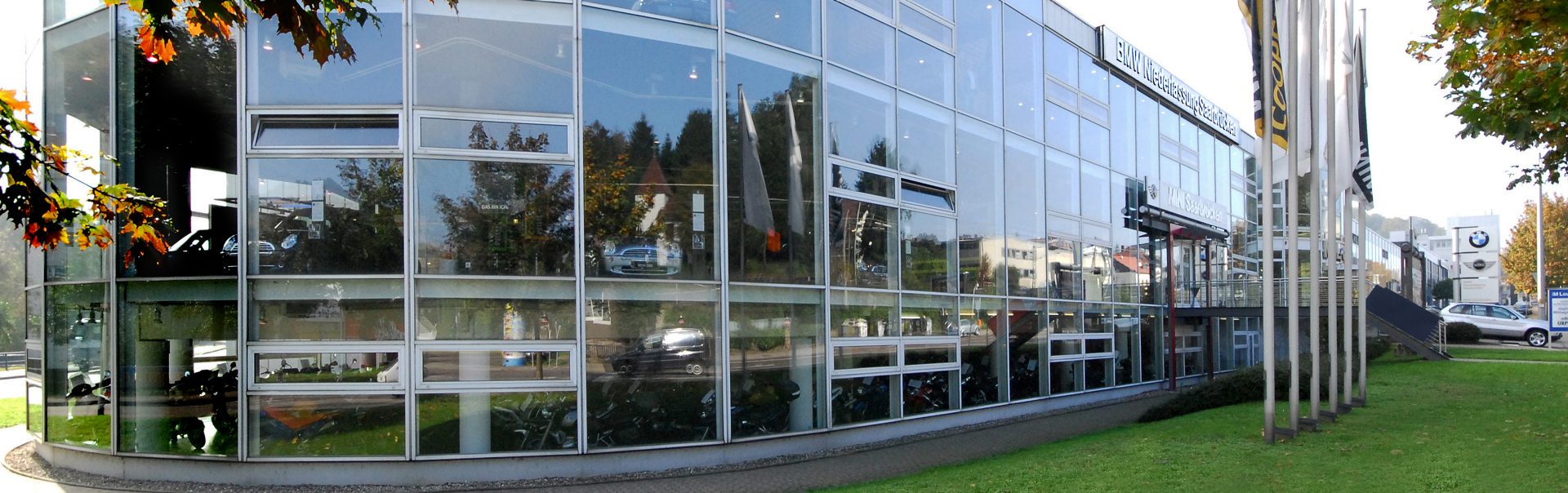 Außenansicht der BMW Niederlassung Saarbrücken mit reflektierenden Fenstern und grüner Umgebung.