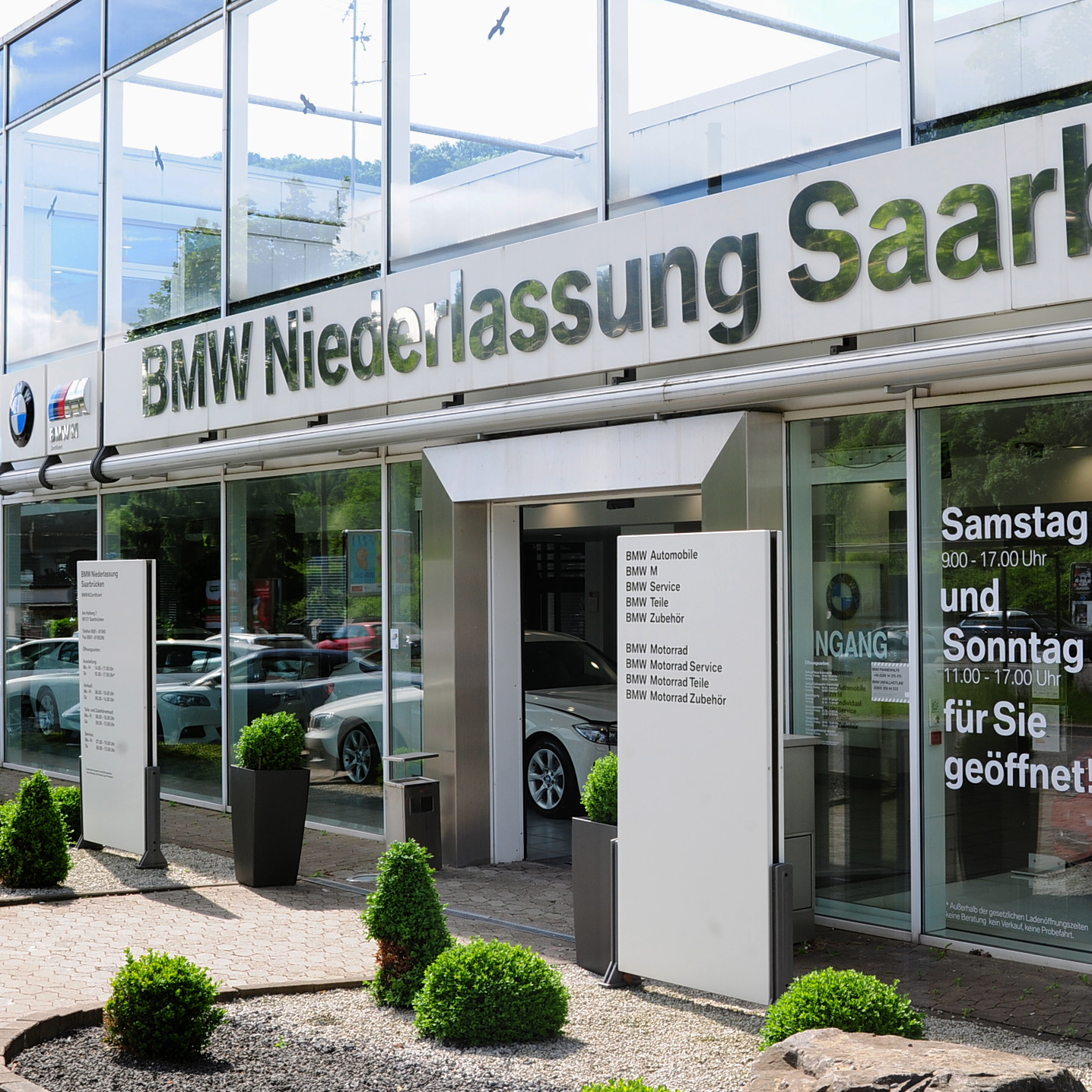 Außenansicht der BMW Niederlassung Saarbrücken mit reflektierenden Fenstern und grüner Umgebung.