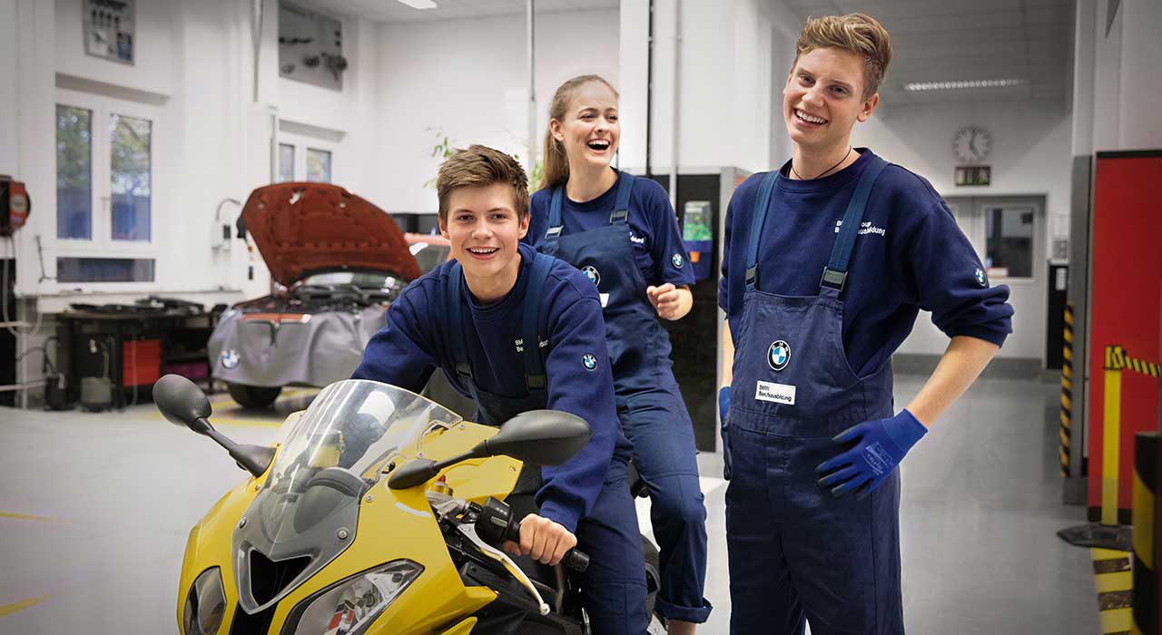 Das Bild zeigt drei lachende Auszubildende in einer BMW Werkstatt.