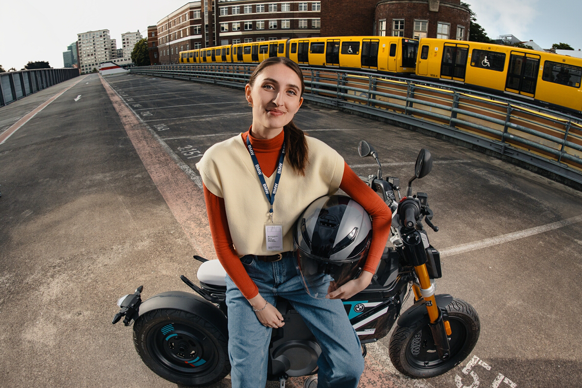 Eine junge Auszubildende der BMW Group sitzt lachend auf einem Scooter