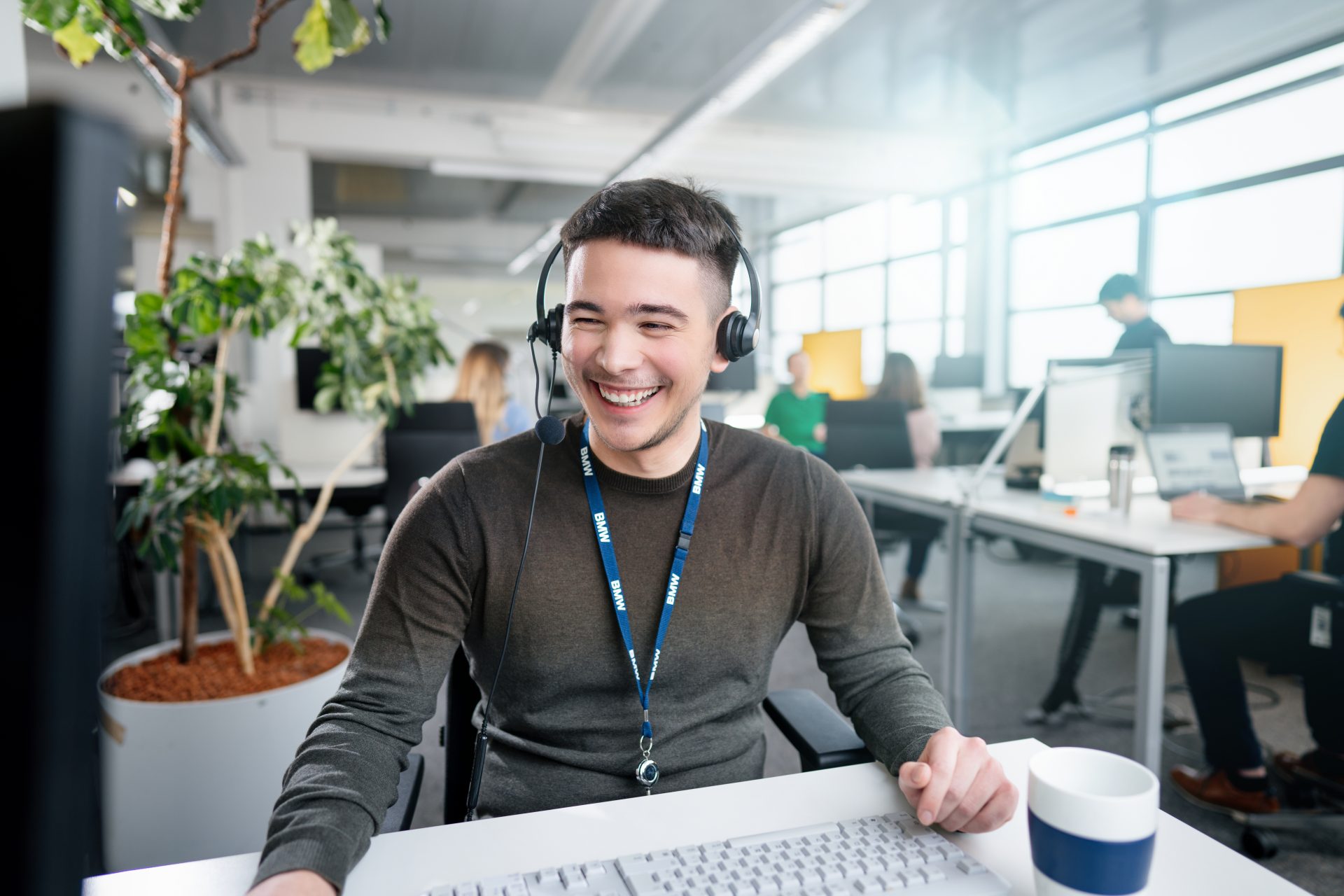 Freundlicher Kundenservice-Mitarbeiter mit Headset in einem modernen Büro bei der BMW Group.