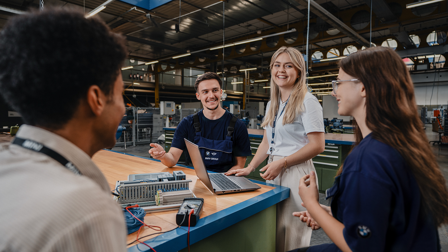 Auszubildende Techniker und Ingenieure arbeiten zusammen an einem Laptop in einer modernen Werkstatt der BMW Group.