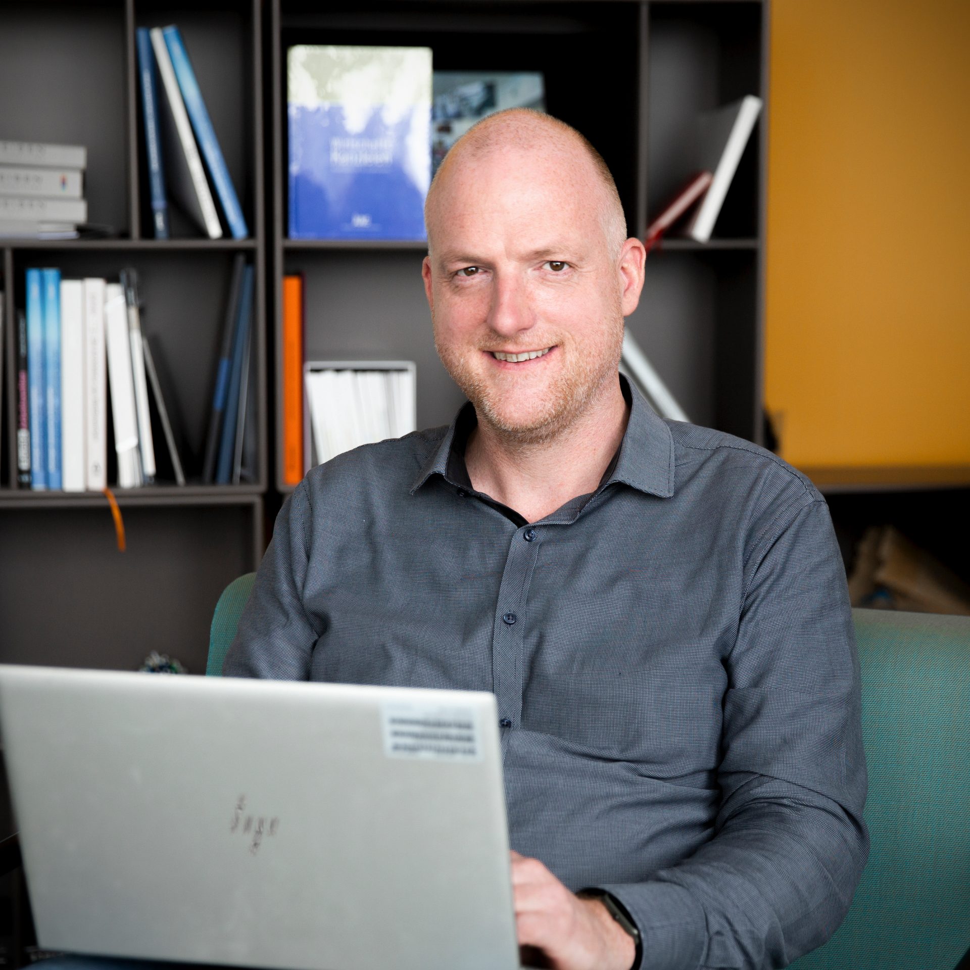Der Recruiter für Ausbildungsberufe arbeitet am LapTop und lächelt in die Kamera.