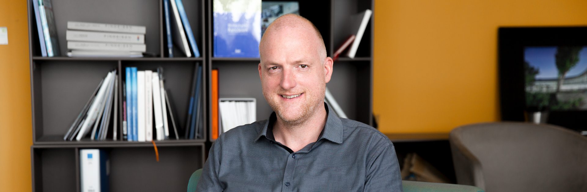 Der Recruiter für Ausbildungsberufe arbeitet am LapTop und lächelt in die Kamera.