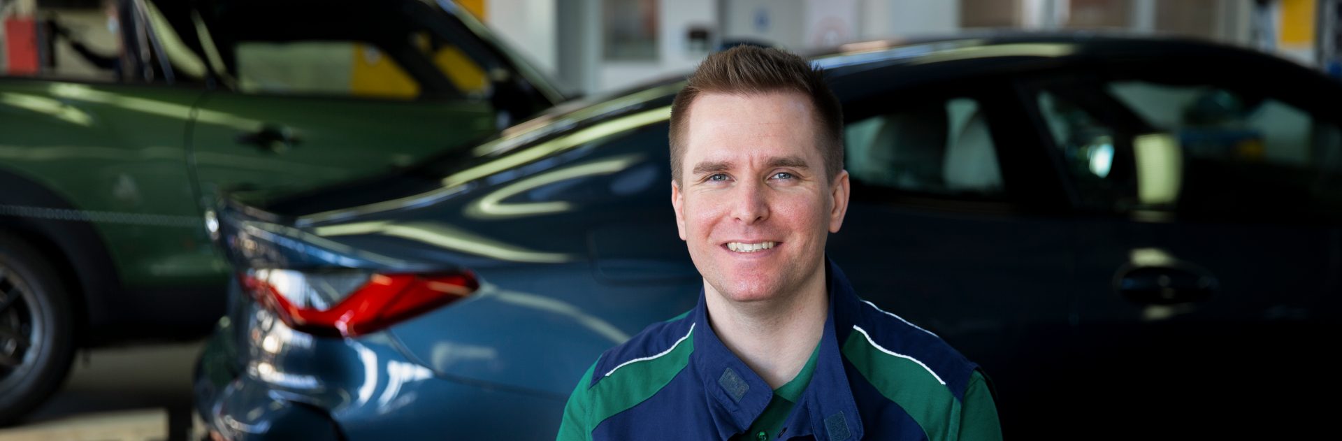 Der Ausbilder für Karosserie und Fahrzeugbau im BMW Group Werk München sitzt vor einem Fahrzeug und lächelt in die Kamera.
