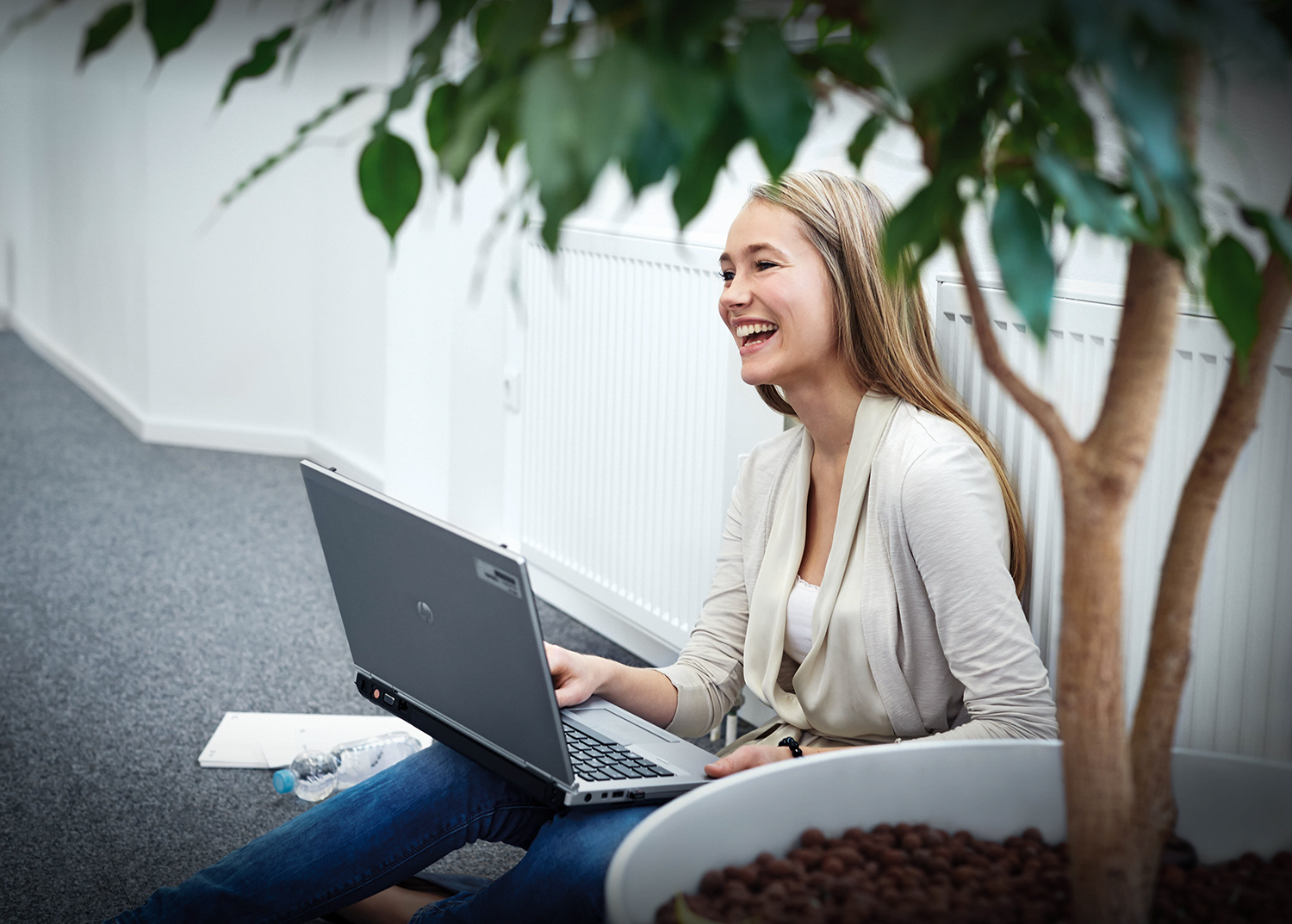 Eine junge Auszubildende der BMW Group sitzt lachend mit ihrem LapTop auf dem Boden.