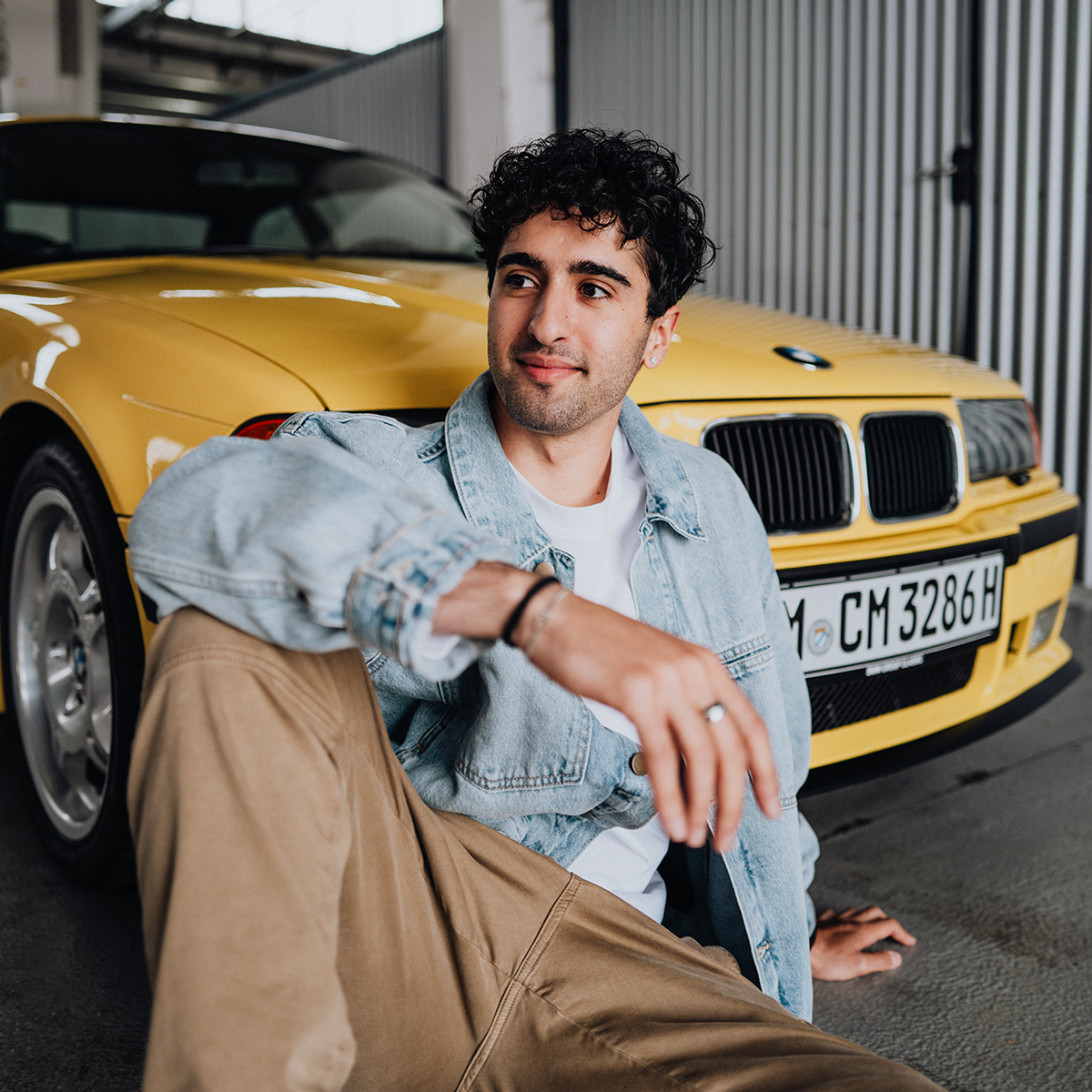 Dualer Student Yasin sitzt am Boden vor einem gelben BMW E36 M3