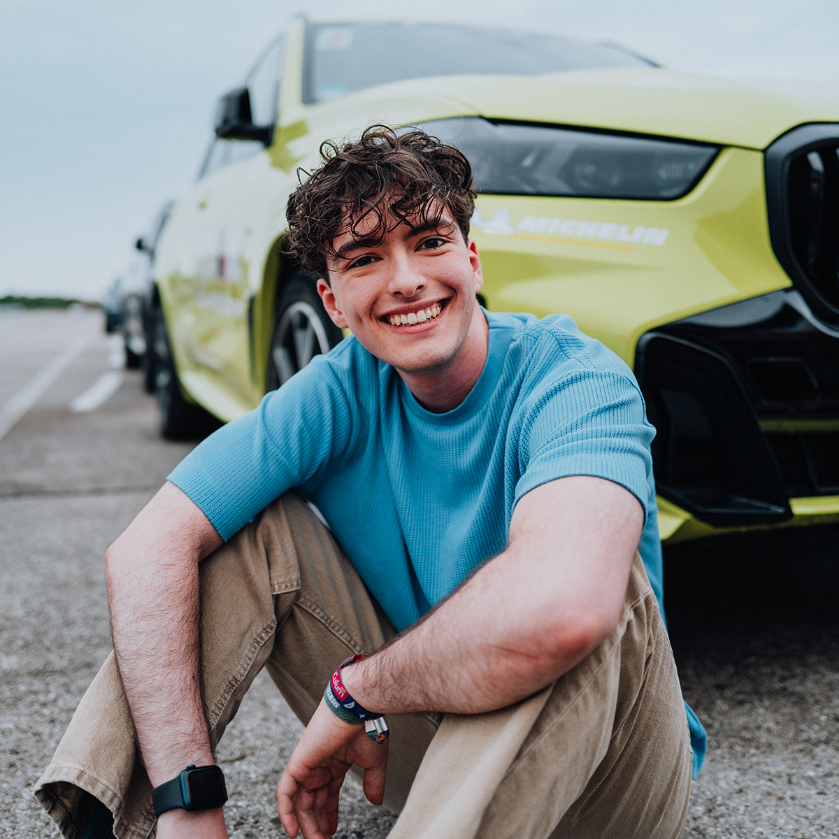 Dualer Student Liam sitzt am Boden vor einem gelben BMW X3M