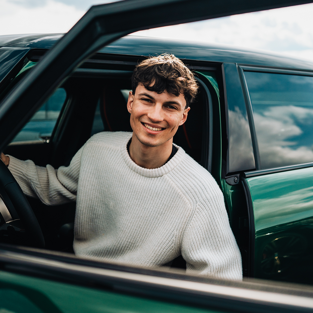 Dualer Student Anton lachend in einem grünen MINI Cooper