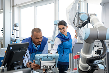 Zwei Mitarbeiter in der Automatisierungstechnik bei der BMW Group arbeiten mit einem Roboter in einem modernen Labor.