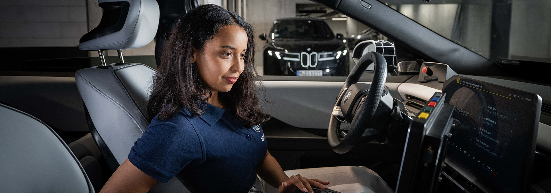 Eine dual Studierende mit Laptop in einem BMW iX3 führt Tests durch