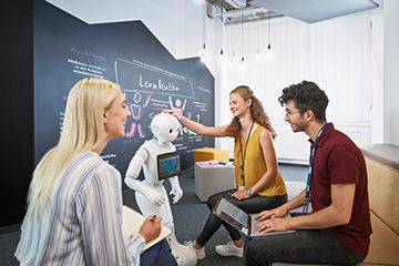 Duale Studenten für Künstliche Intelligenz bei der BMW Group interagieren mit einem Roboter in einem modernen Büro.