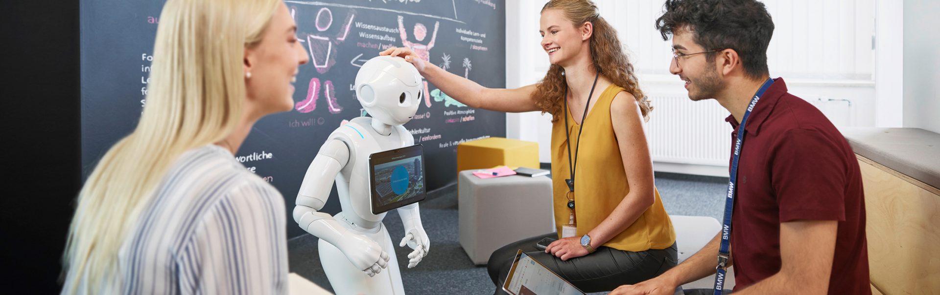 Duale Studenten für Künstliche Intelligenz bei der BMW Group interagieren mit einem Roboter in einem modernen Büro.