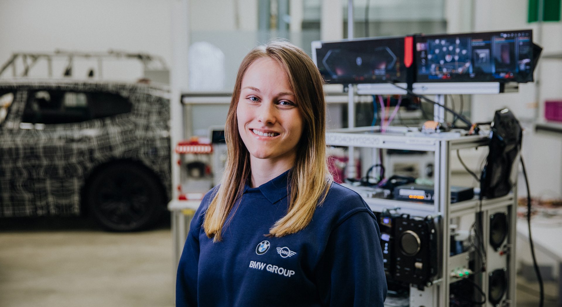 Eine Duale Studentin für Künstliche Intelligenz steht in einer Werkstatt und lächelt in die Kamera.