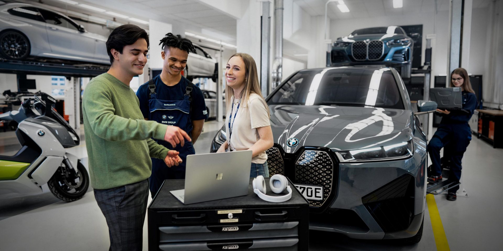 Drei Auszubildende am Laptop vor einem BMW iX in einer Werkstatt bei der BMW Group.