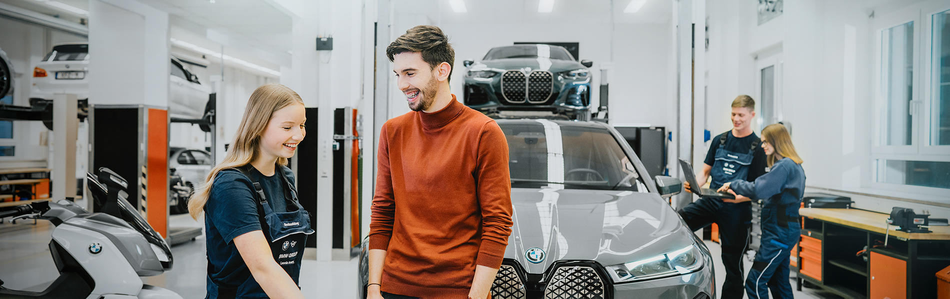 Zwei Azubis unterhalten sich in einer BMW Group Werkstatt mit einem BMW iX im Hintergrund.