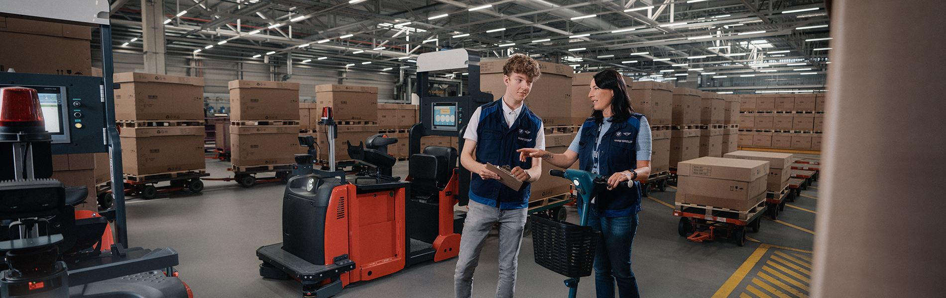 Zwei Azubis unterhalten sich in einer BMW Group Werkstatt mit einem BMW iX im Hintergrund.